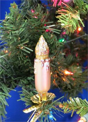 Vintage pink glass Christmas light bulb ornament with gold flame tip and base, hanging on a green tree branch.