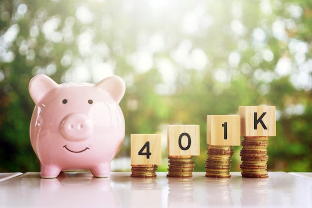 Pink piggy bank beside wooden blocks spelling "401K" stacked on coins, symbolizing retirement savings planning.