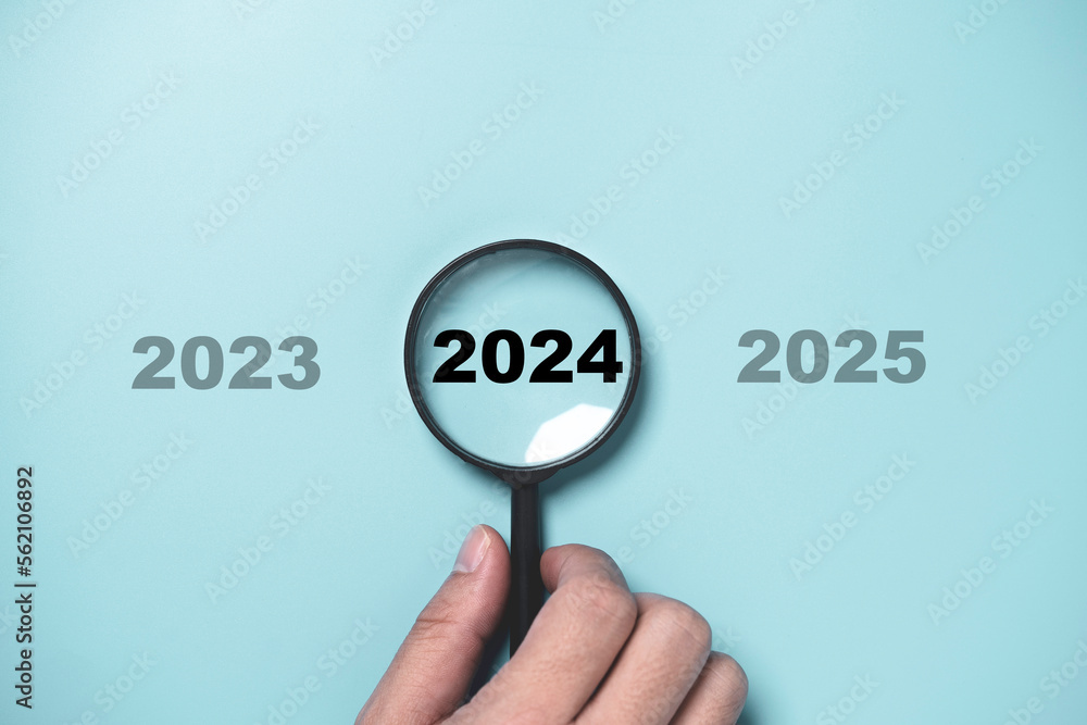 Hand holding black magnifier glass with 2024 year among 2023 and ...