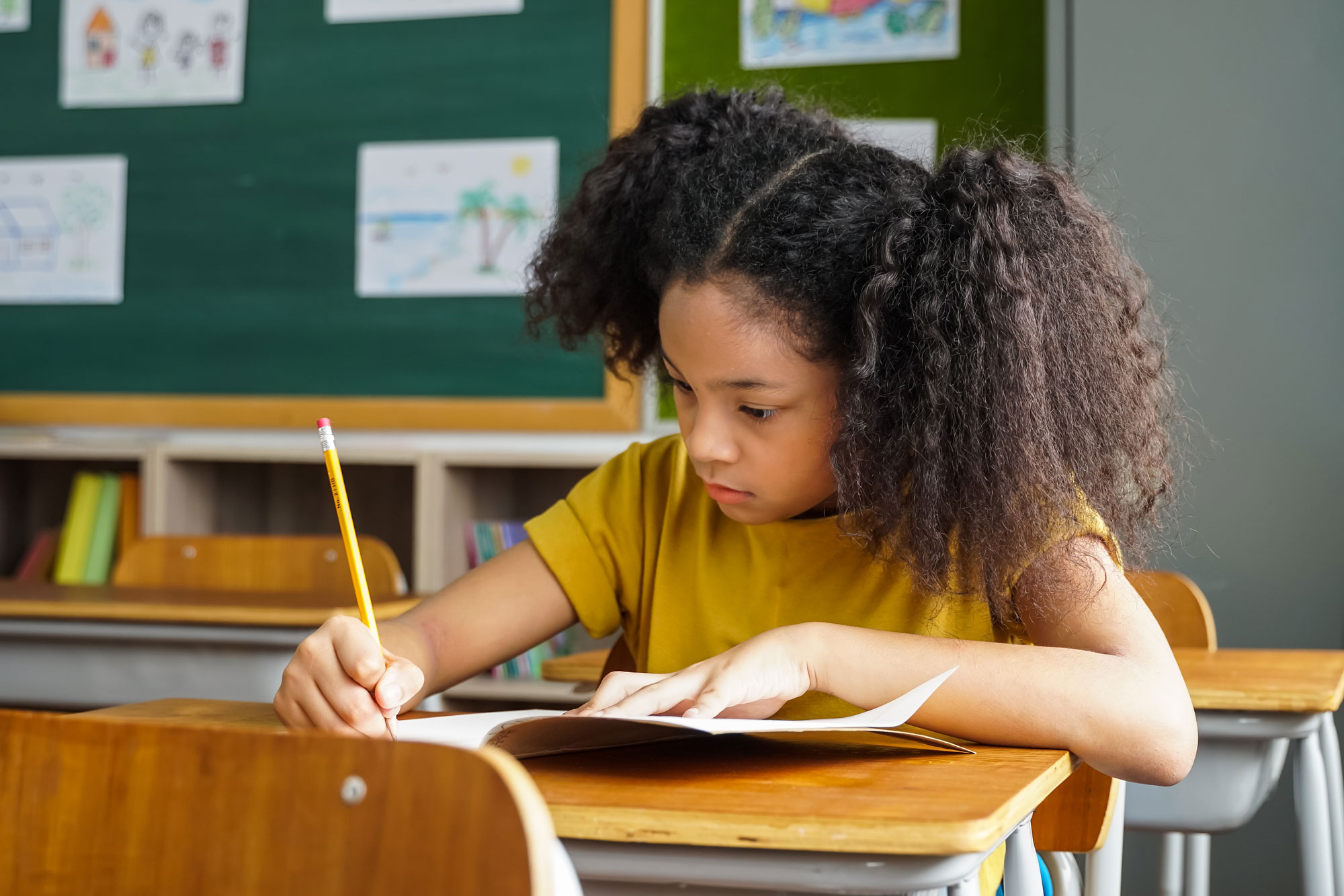 Elementary School Student Sitting at Desk in Classroom and Writing ...