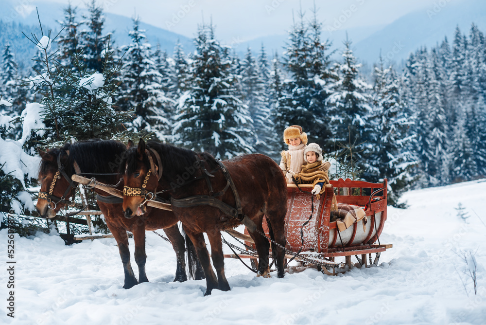 Poster, Wandbilder Two children ride on a retro sleigh with horses in  winter time, 40x26.7 cm