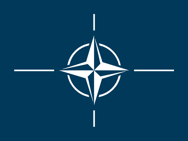 NATO emblem - white four-pointed compass rose on dark blue background, symbolizing unity and collective defense.