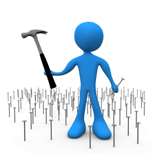 Blue 3D figure holding a hammer stands among scattered nails, symbolizing construction or problem-solving.