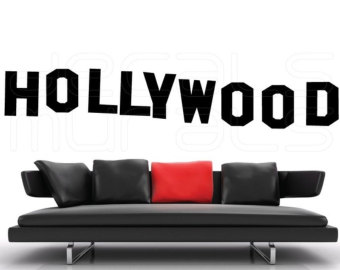 Modern black sofa with red accent pillow beneath bold "HOLLYWOOD" text on white background.