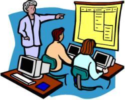 Instructor teaching computer skills to two students in a classroom setting with desktop computers and a whiteboard.