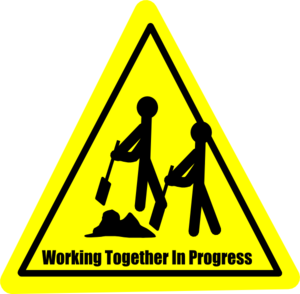 Yellow triangular warning sign showing two stick figures digging together with text "Working Together In Progress".