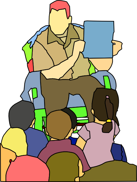 A teacher with red hair holds up a blue book while reading to a diverse group of seated children.