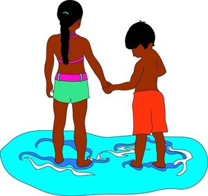 Two children holding hands while standing in shallow water, smiling and playing together.