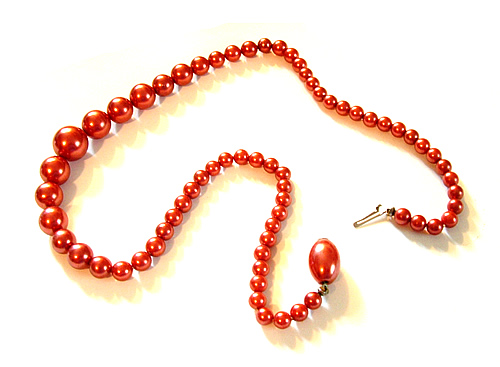 A vibrant red pearl necklace with matching pendant and silver-toned clasp, arranged elegantly on a white background.