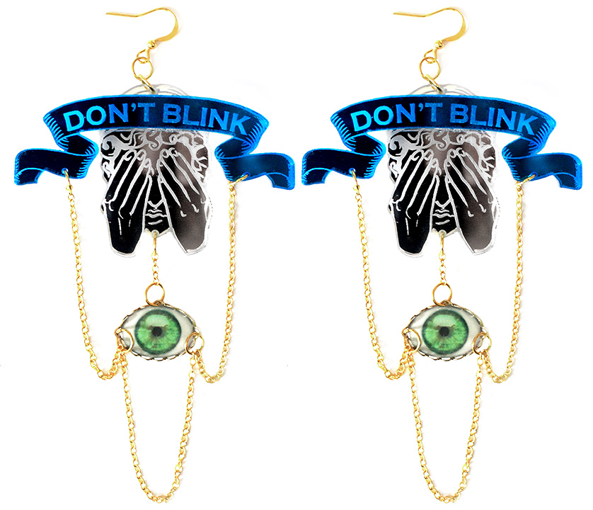 Pair of "DON'T BLINK" earrings featuring Weeping Angel silhouette, blue banner, and dangling green eye charm on gold chain.