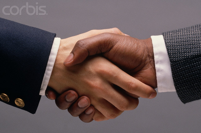 Two professionals of different ethnicities shaking hands in a formal business setting.
