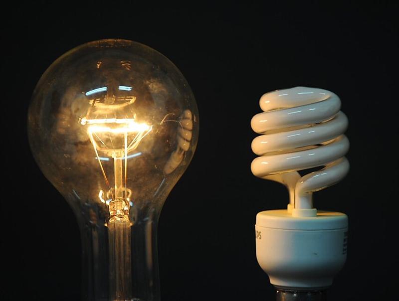 Incandescent and compact fluorescent light bulbs side by side against a black background, illustrating energy efficiency comparison.