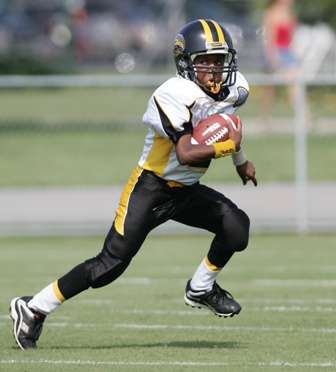 Young football player in yellow and black uniform sprinting with ball during youth game.