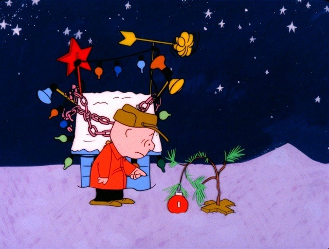 Charlie Brown gazes sadly at a small, sparsely decorated Christmas tree under a starry night sky.