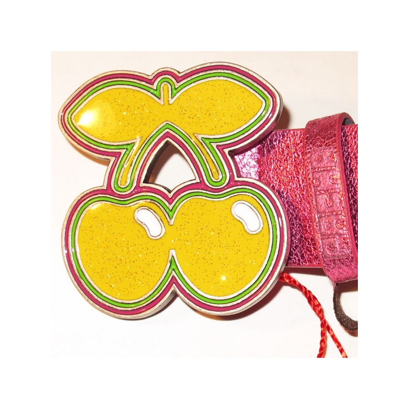 Bright yellow cherry-shaped enamel pin with pink and green outlines, attached to a shimmering pink leather strap.