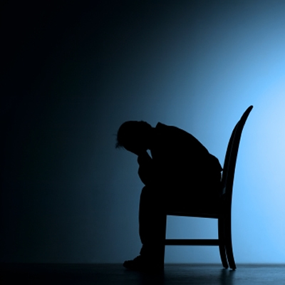 Silhouette of a person slumped in a chair, head in hands, against a blue gradient background-symbolizing sadness or depression.