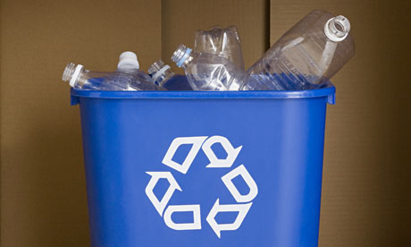 Blue recycling bin filled with clear plastic bottles, featuring a white universal recycling symbol on the front.