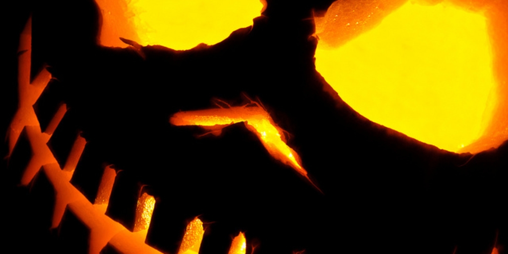 Glowing jack-o'-lantern with menacing carved eyes, nose, and jagged teeth lit from within by warm orange light.