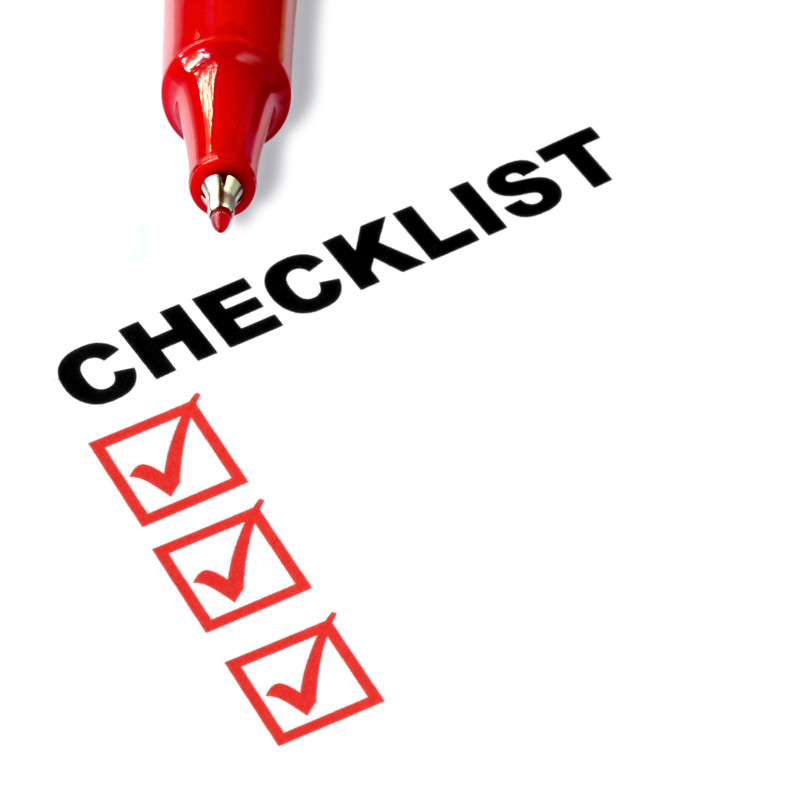 Red pen poised over a checklist with three checked boxes on white paper.