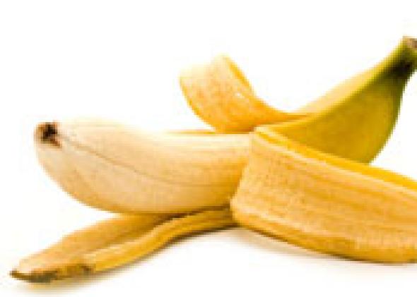A peeled banana with its yellow peel scattered beside it on a white background.