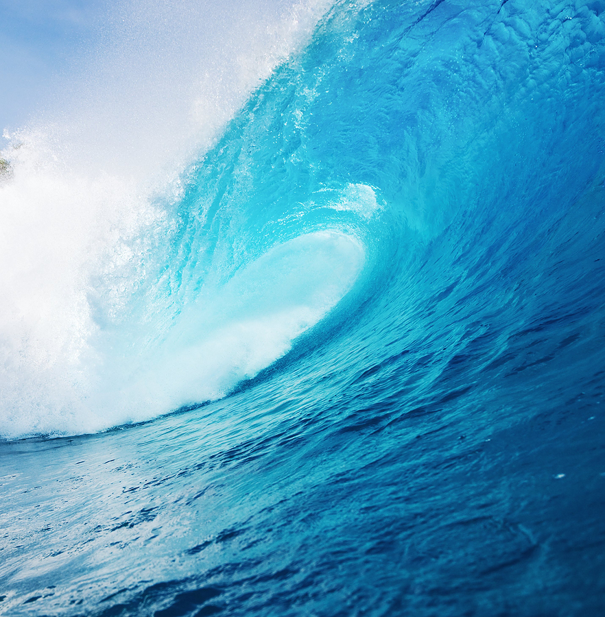 A powerful turquoise ocean wave curling into a perfect barrel under bright sunlight, with white foam spraying at the crest.