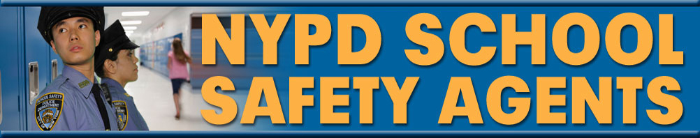 Two NYPD School Safety Agents in uniform standing in a school hallway with students walking in the background.