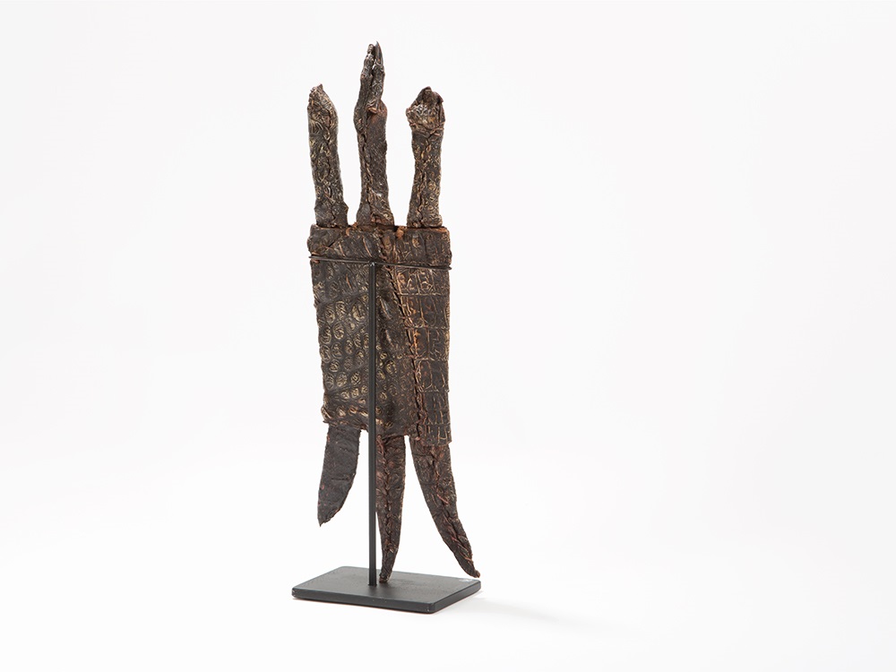 Ancient carved wooden artifact with three upright prongs and intricate geometric patterns, displayed on a black stand against white background.