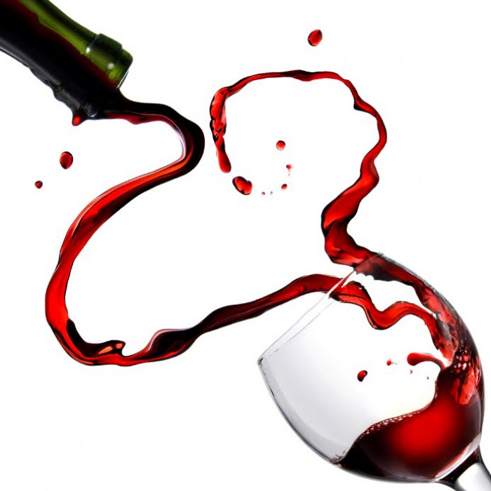Red wine dramatically splashing from a green bottle into a clear glass against a white background.