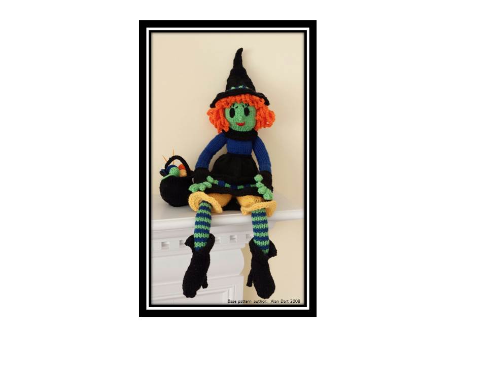 Hand-knitted witch doll with green face, orange hair, black hat, striped socks, and a small cauldron, sitting on a white mantel.