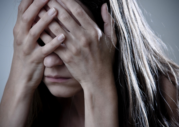 Woman covering her face with hands, expressing distress or anxiety against a neutral background.