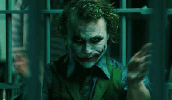 The Joker behind prison bars, grinning maniacally with green hair and smeared makeup, wearing a vest and shirt.