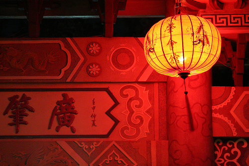 Glowing red Chinese paper lantern with dragon motifs hanging beside a traditional carved wooden plaque with Chinese characters.