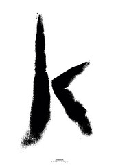 Bold black ink brushstroke forming the letter "K" on white background, expressive and abstract.