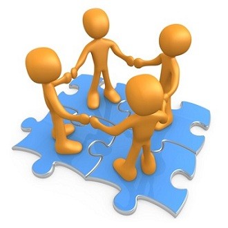 Four orange 3D figures standing on blue puzzle pieces, holding hands in a circle to symbolize teamwork and collaboration.