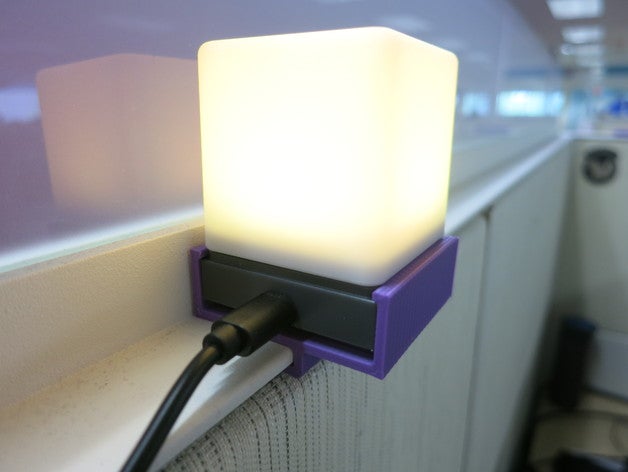 A glowing cube-shaped lamp with a purple holder attached to a wall, plugged in and emitting soft light.