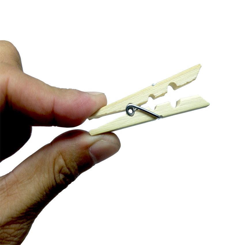 A hand holding a small wooden clothespin with a metal spring against a white background.