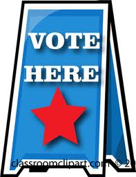 Blue "VOTE HERE" sign with red star, standing on a sidewalk.